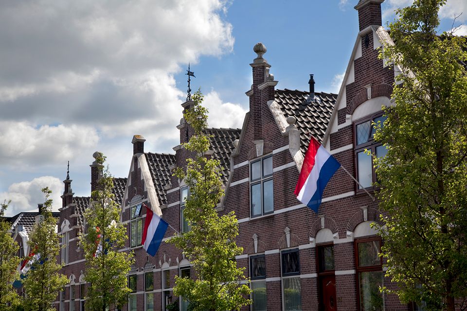 Historische huizen met sierlijke gevels en wapperende Nederlandse vlag in Woerden – een trots en sfeervol straatbeeld vol Hollandse charme.