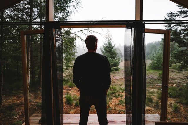 Een man staat in de deuropening van een vakantiehuisje midden in de natuur.