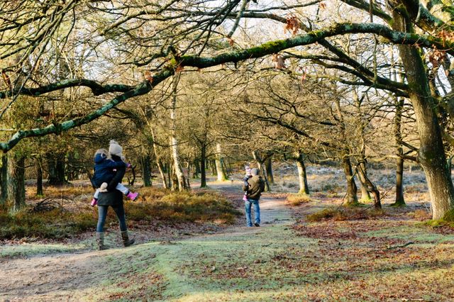 Een man en vrouw lopen in de winter met elk een kind op de arm door de natuur.