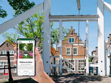 Een smartphone met de website van Laag Holland met op de achtergrond een foto van Edam.