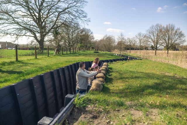 Kinderen met ouders in een loopgraaf omgeven door groen en wijds uitzicht.