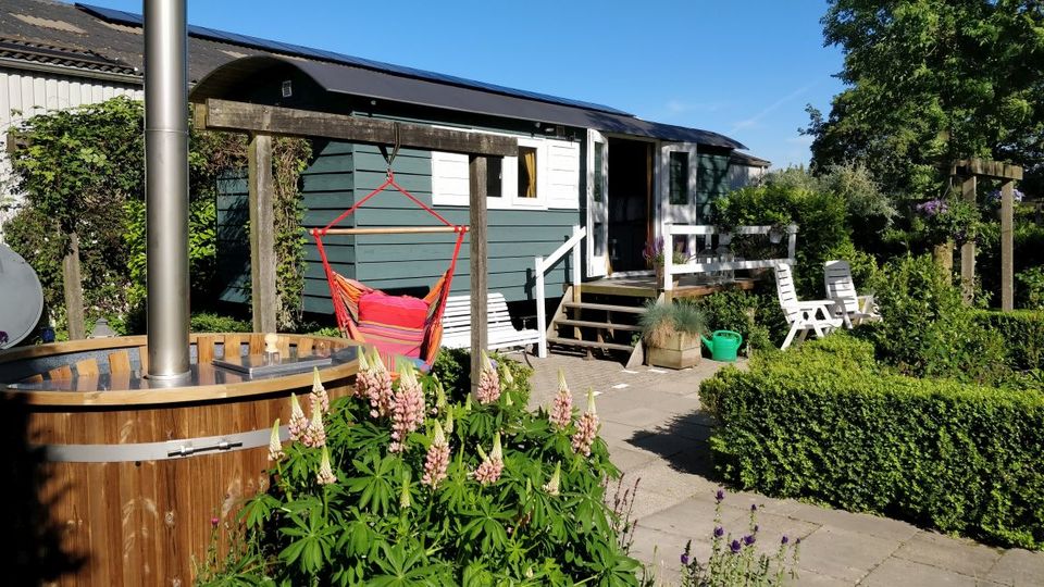 Een klein huisje op wielen omringt door groen. Voor het huisje staat een hottub en een hangmat. In Ens in de Noordoostpolder.
