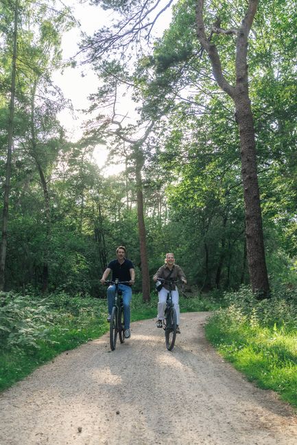 Een man en vrouwen fietsen over grindpad door het groene bos