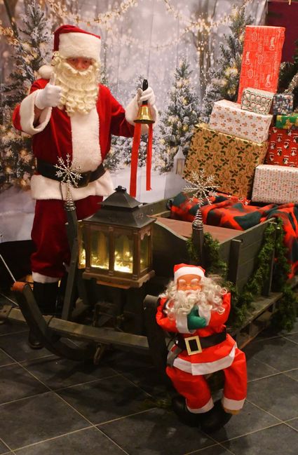 Kerstman tijdens de kerstmarkt in de Sint-Franciscuskerk in Oudewater, Groene Hart, met een kerstbel, verlichte lantaarn, ingepakte cadeaus en feestelijke kerstdecoratie.