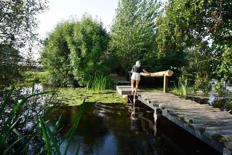 Groepsactiviteit op het blotevoetenpad bij Buitenplaats Kameryck in Kamerik, waar een vrouw over een houten brug door de natuur loopt