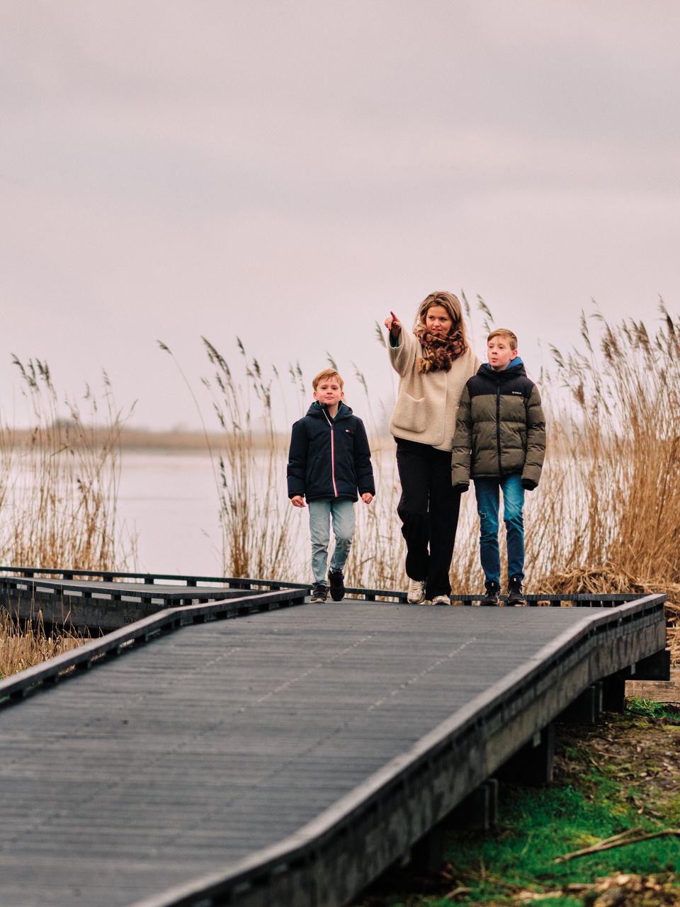 Een vrouw en twee kinderen wandelen in warme kleding over een steigerpad in Nationaal Park Nieuw Land