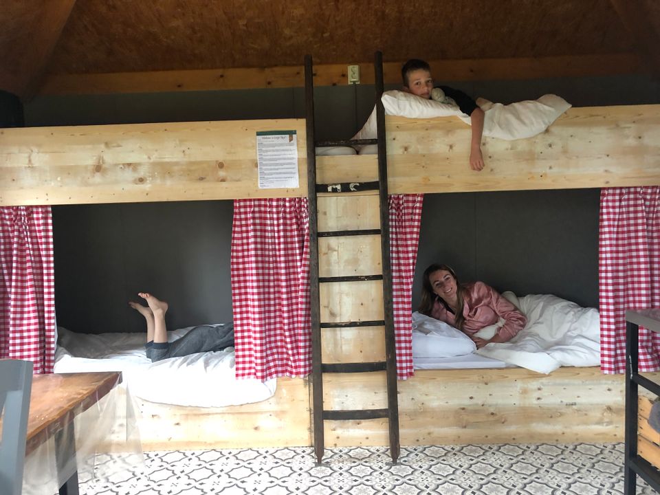 Binnenzijde van een groepsaccommodatie bij BoerBert met houten stapelbedden, rode gordijntjes en kinderen die overnachten op de boerderij in het Groene Hart.