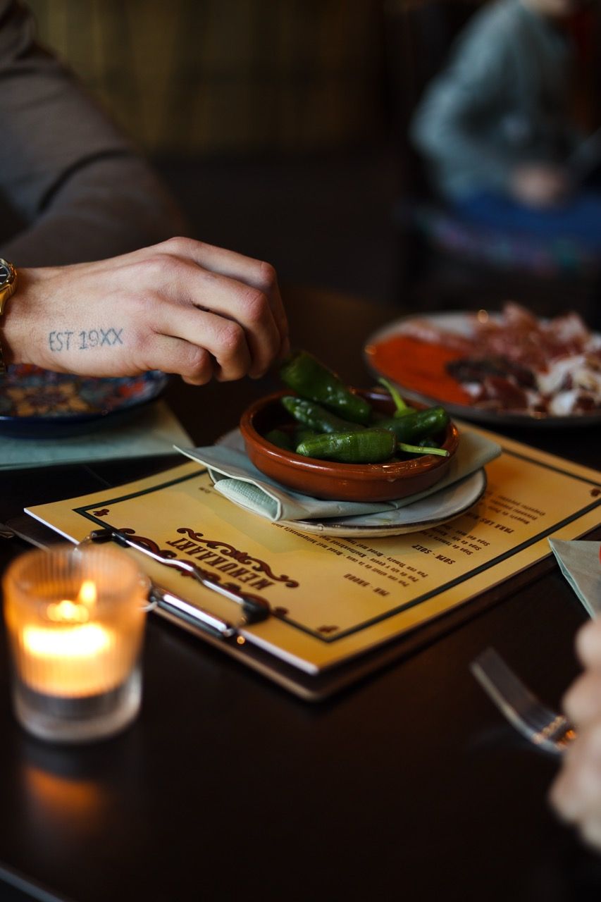 Je ziet een hand groene pepers pakken die in een schaaltje zitten.