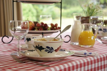 Tafel gedekt met Brabants bont tafelkleed en servies, met een fruitschaal en karaf met jus d'orange en melk.