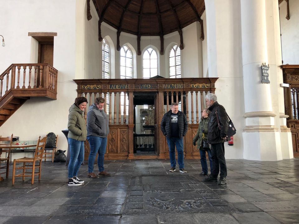 Vijf personen staan in een kerk en luisteren naar een gids.