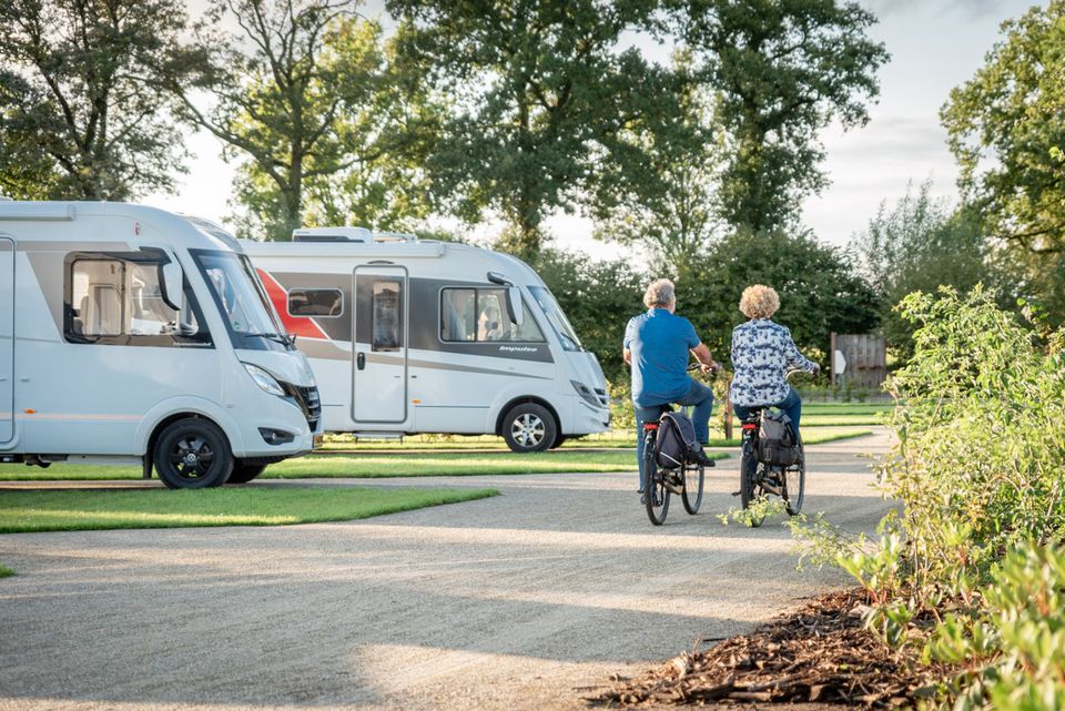 2 campers op een standplaats en 2 fietsers op een gravelpad.