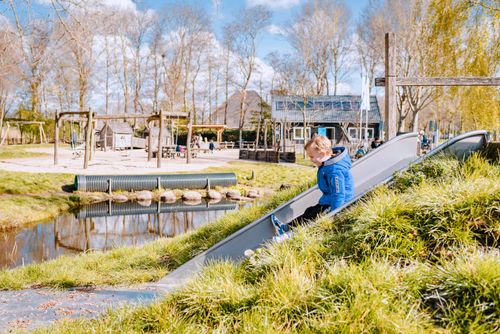 Spelende kinderen in speeltuin, kind van glijbaan met blauwe jas