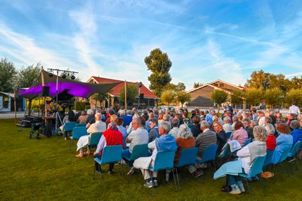Publiek op blauwe stoelen kijkt naar een kleinschalig openluchttheater met paarse doeken op Buitenplaats Kameryck tijdens een Midzomeravondvoorstelling.