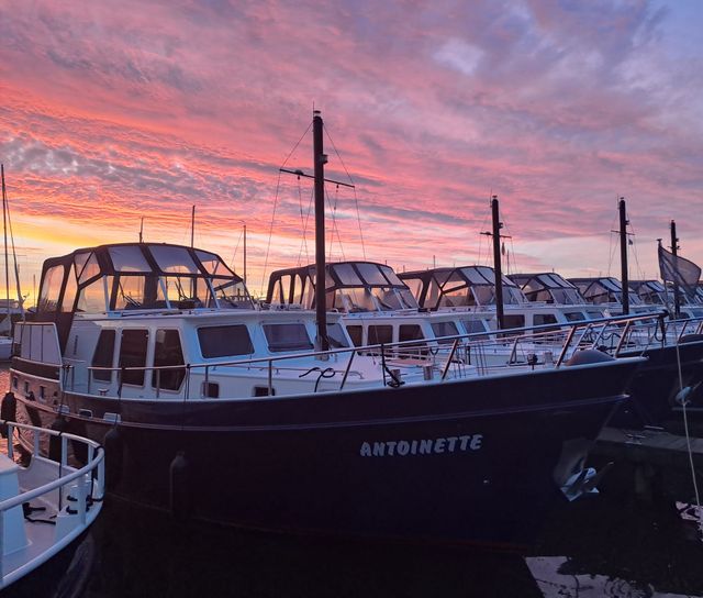 Meerdere motorjachten van Yachtcharter De Drait op een rijtje in de haven met een mooie zonsondergang op de achtergrond.