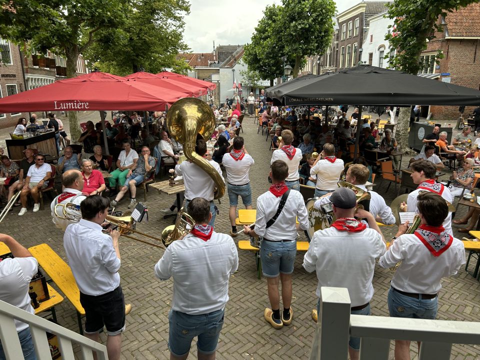 Stedelijk plein De Markt in Oudewater, Groene Hart, Muziek op de Markt met live blaaskapel en volle terrassen tijdens zomers evenement op historisch stadsplein.