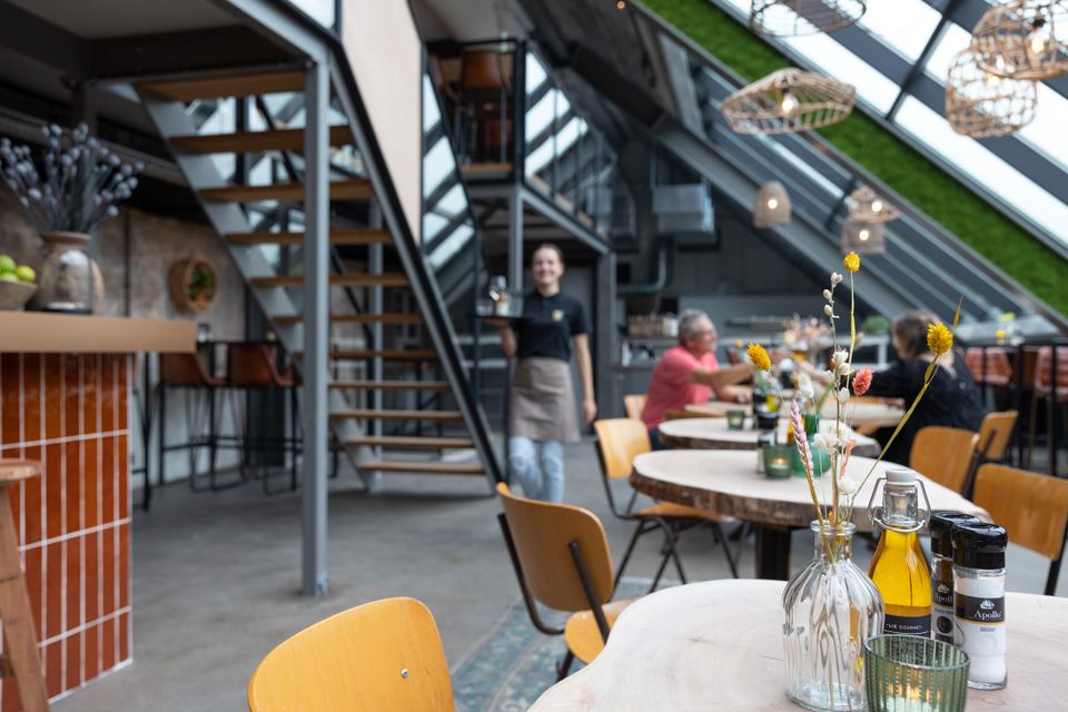 Bezoekers zitten aan een tafeltje in Fort de Gagel terwijl er een serveerster langsloopt.
