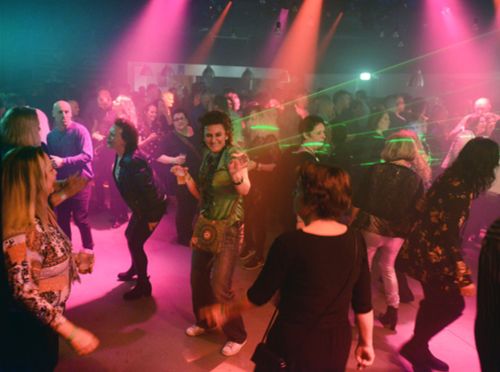 Foto van mensen op dansvloer met gekleurde lampen en lasers.