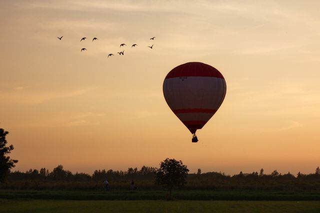 Een luchtballon in de lucht met vogels en een zonsondergang.