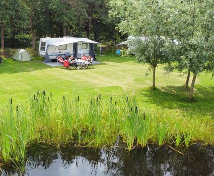 Kampeerplaats van De Gerrithoeve met op de voorgrond een vijver en op de achtergrond caravans op en groen veld met bomen.
