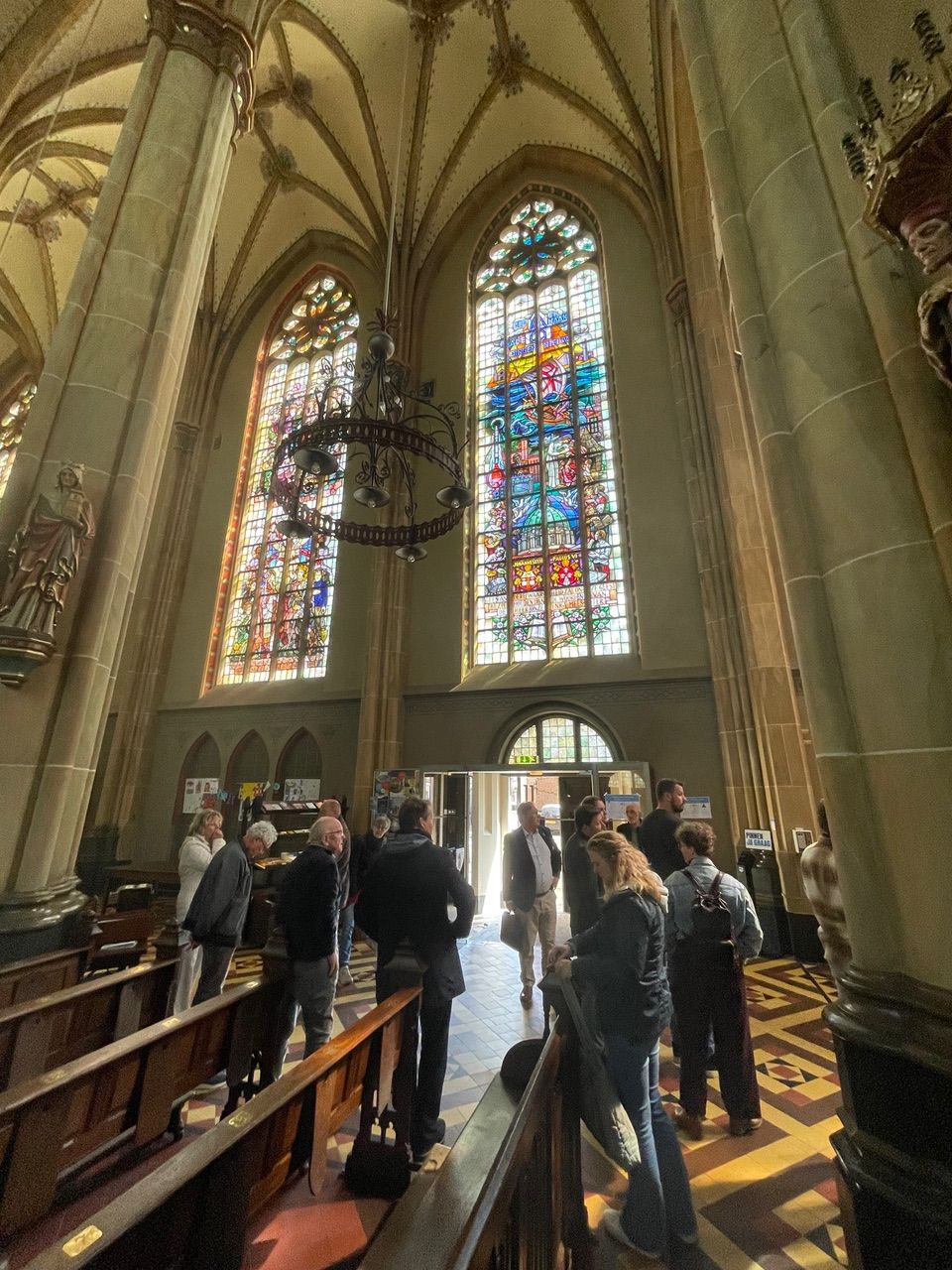 Mensen kijken rond in de basiliek van Ijsselstein met glas-in-lood ramen op de achtergrond