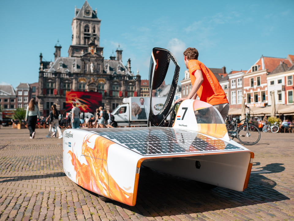 Student van de TU Delft lopend met de Nuna op de Markt in Delft