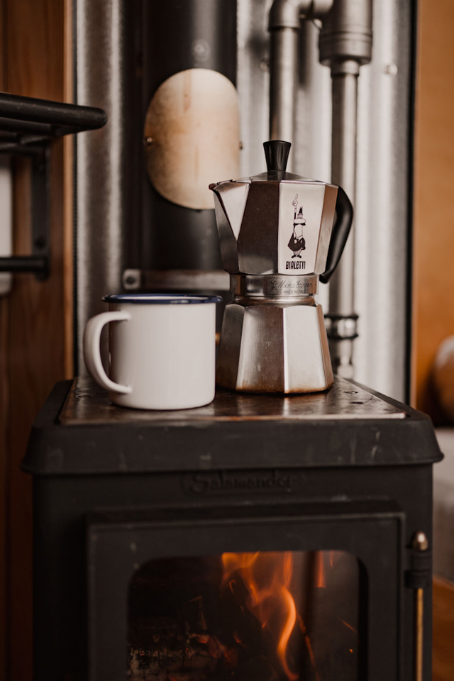 Ein Foto von einer Kaffeekanne und einer Tasse, die auf einem Holzofen in einem Ferienhäuschen in Drenthe stehen.