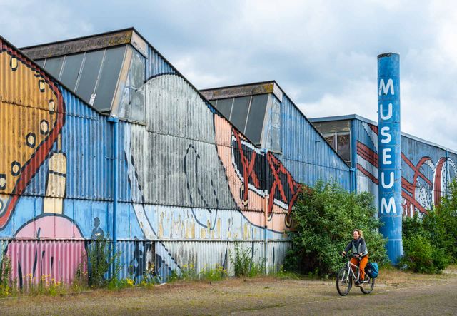 Een fietsers naast een felgekleurd gebouw met muurschilderingen.