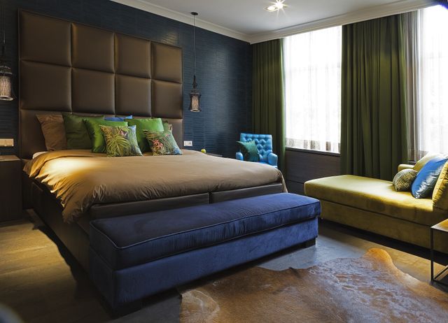 Chique hotelkamer met kingsize bed, goudkleurig met blauwe accenten en een chaise longue.