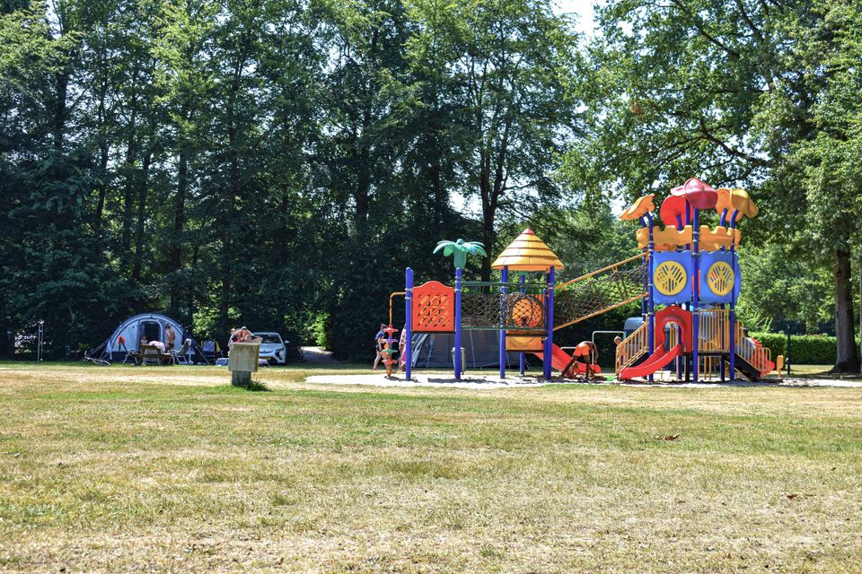 Een kleurrijk speeltoestel op een groot grasveld, eromheen staan tenten. In Kraggenburg in de Noordoostpolder.