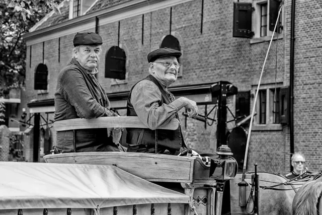 Historische Kaasmarkt in Woerden, regio Groene Hart, met twee mannen in traditionele kleding op een paard en wagen langs monumentale panden in de binnenstad.