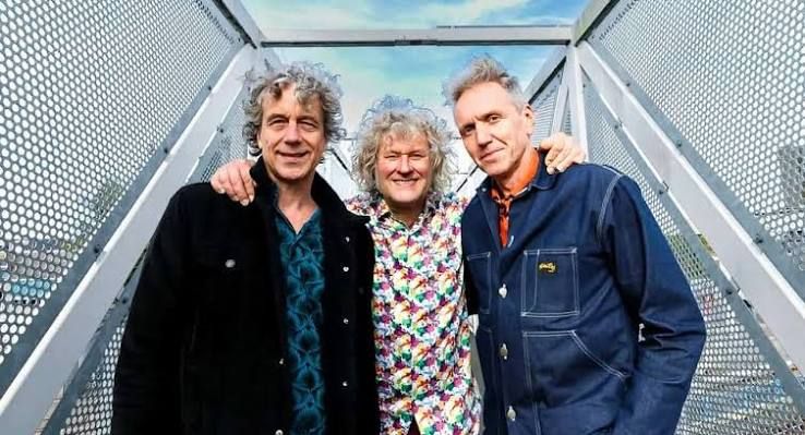 Foto van drie artiesten met armen om elkaar heen in een soort stalen kooi.
