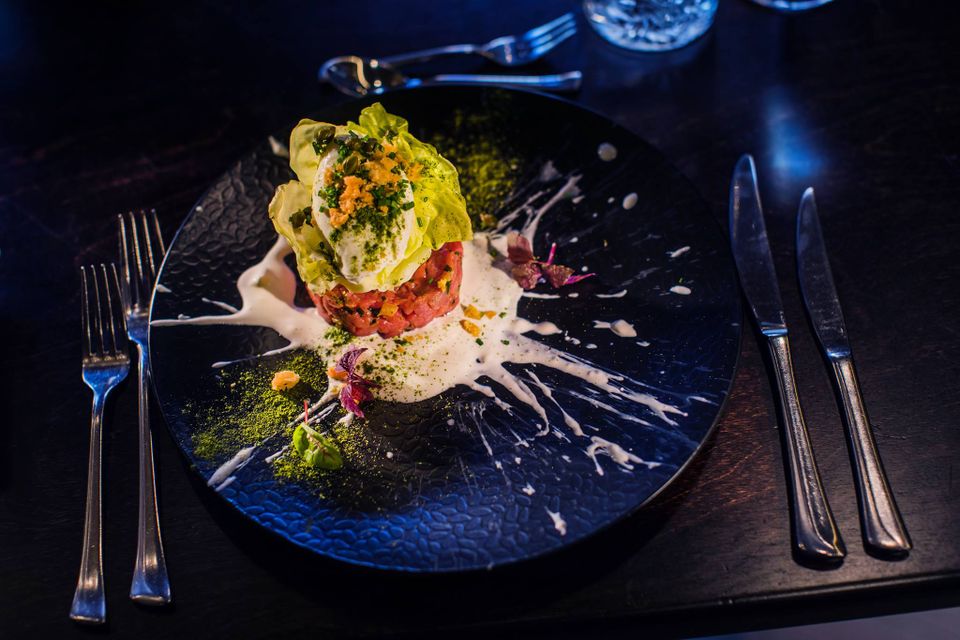 Geraffineerd gerecht bij restaurant De Heeren van Montfoort met steak tartaar, zachtgegaard ei, groene kruiden en romige saus, stijlvol gepresenteerd op een donker bord.