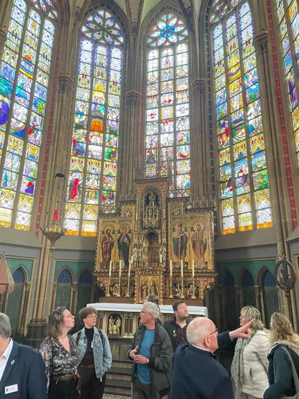 Rondleiding in basiliek Ijsselstein, kleurrijke glas-in-loodramen op de achtergrond.