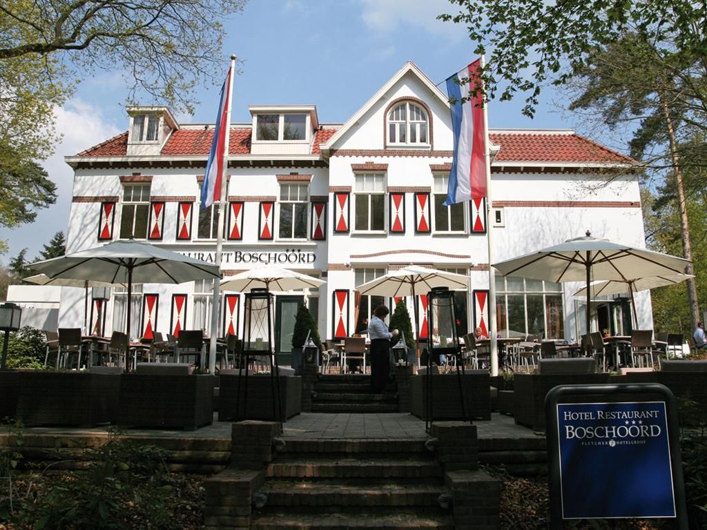 Foto van een witte voorgevel van het hotel met rood-witte luiken en op de voorgrond het terras met parasols.