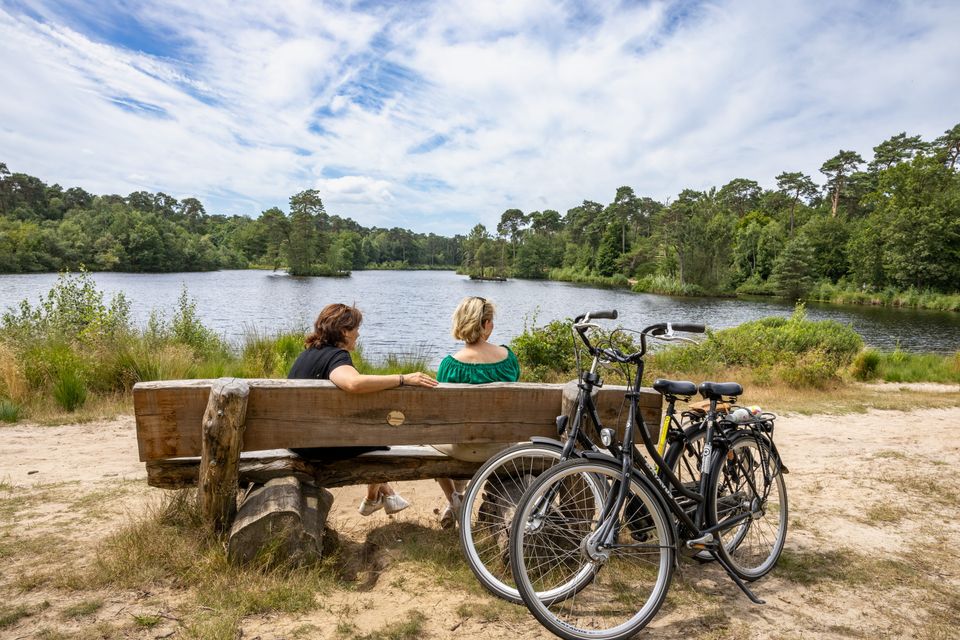 Twee vrouwelijke fietsers zitten op een bankje te genieten van het uitzicht over het Van Esschenven in Osterwijk. Hun fietsen staan tegen het bankje.