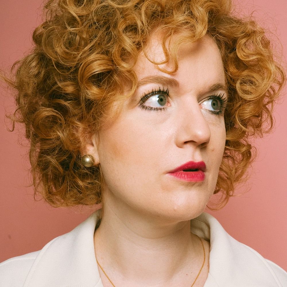 Close-up foto van Anne-Marije met haar enorme krullenbol tegen een roze achtergrond.