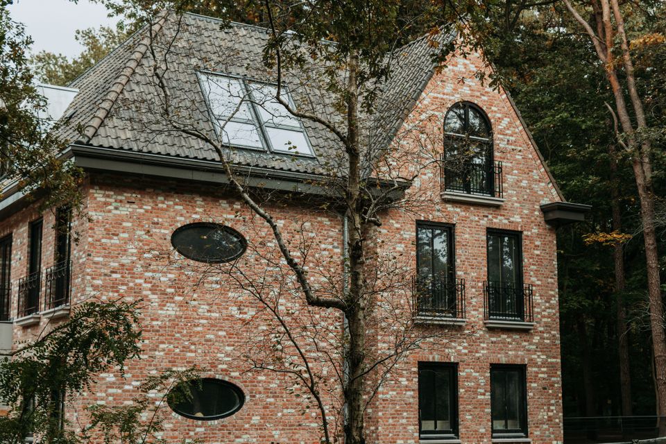 Zijgevel van het hotel met roze baksteen tegen een bosrijke achtergrond.