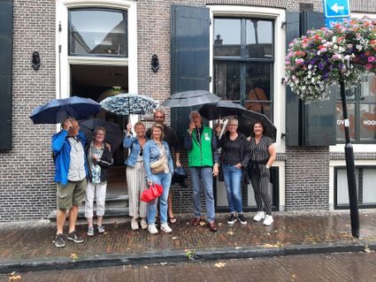 Instapwandeling met stadsgids door de historische binnenstad van Woerden, Groene Hart, met een groep deelnemers onder paraplu’s voor een monumentaal pand.