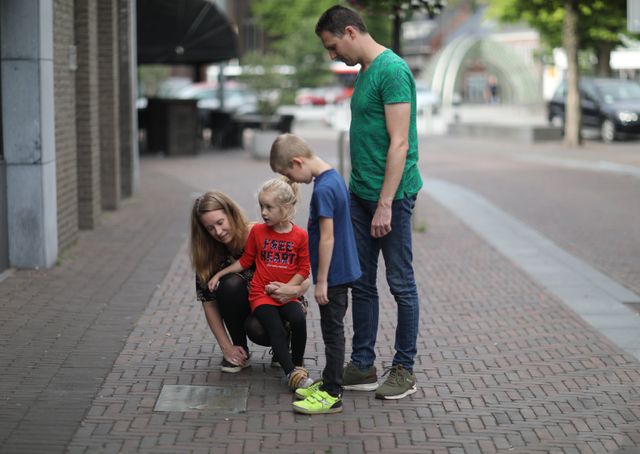 een gezin met kinderen bekijkt een bronzen plaquette in de straten van Asten