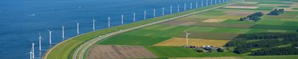 Luchtfoto van dijk met windmolens op water.