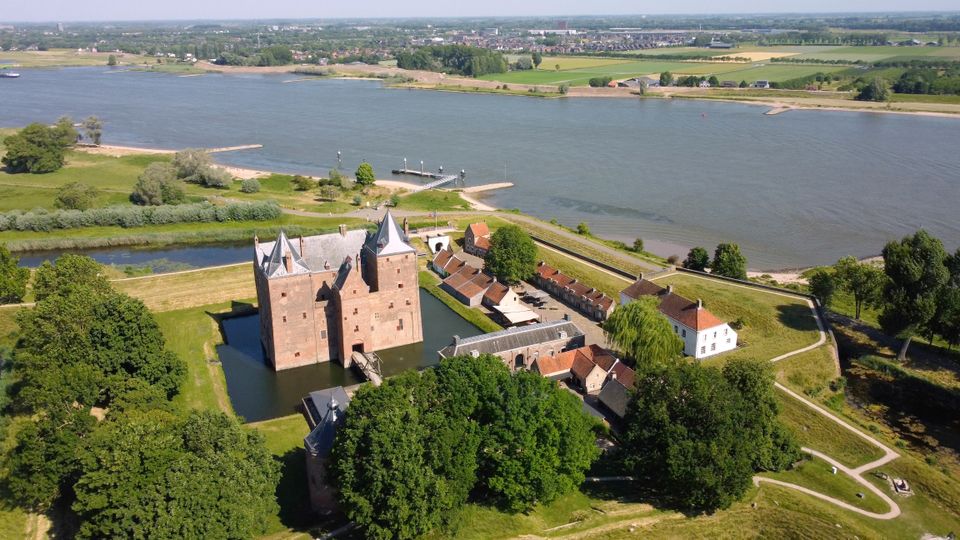 Een groot kasteel aan een rivier, omringd door veel groen.