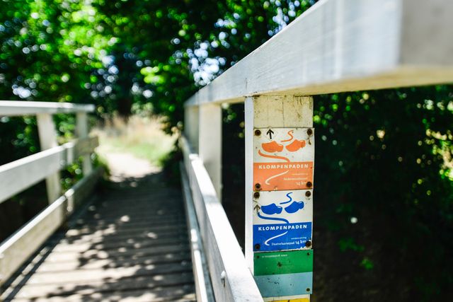 Wandelmarkeringen van de Klompenpaden op een houten brug op de Utrechtse Heuvelrug. De foto toont onder andere het Nederwoudsepad en Daatselaarsepad en verwijst naar wandelen door het groene buitengebied.