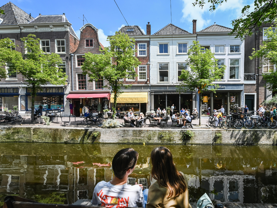 Een koppel dat aan de grachten aan het lunchen is met aan de andere kant van de gracht gezellige terrasjes en winkels