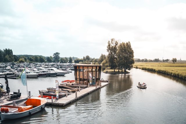 Jachthaven Marnemoende in IJsselstein, Groene Hart. Moderne jachthaven met aanlegsteigers, sloepen en motorboten aan het water, terwijl een recreatieboot over de Hollandsche IJssel vaart langs het groene polderlandschap.