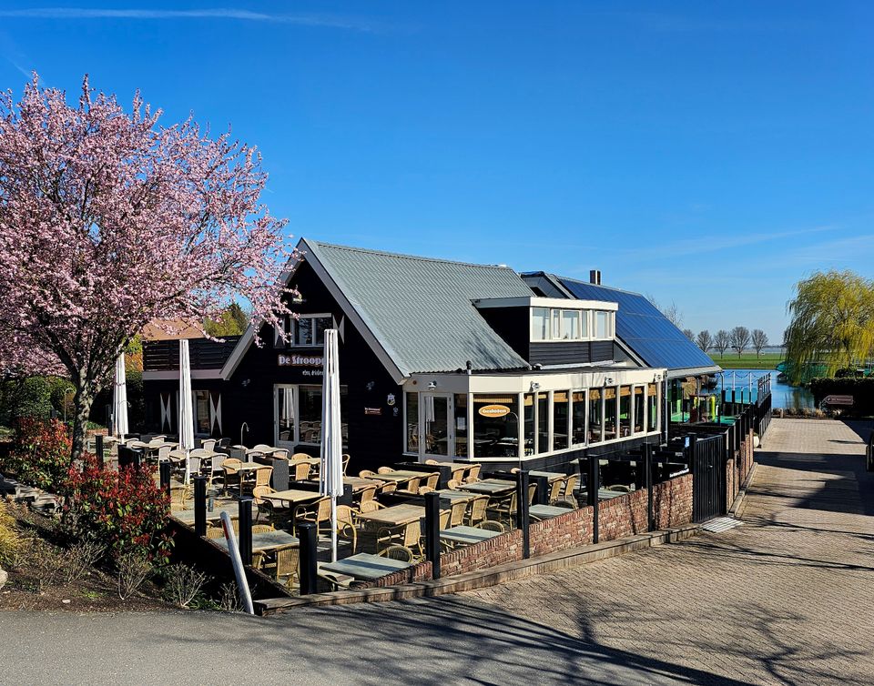 Restaurant De Strooppot in De Hoef, Groene Hart. Landelijk gelegen restaurant met groot terras aan het water, bloeiende boom en uitzicht over het polderlandschap.