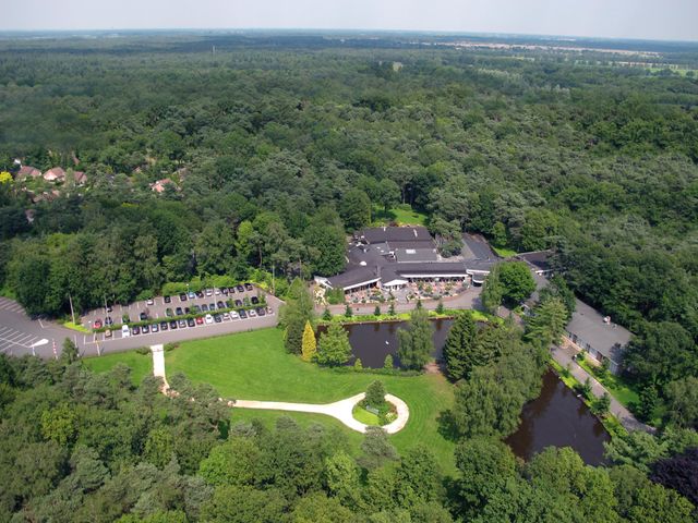 Luchtfoto van de bossen met in het midden een groot grasveld en het hotel-restaurant.