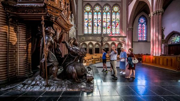 groep mensen krijgt uitleg bij preekstoel met houten beelden