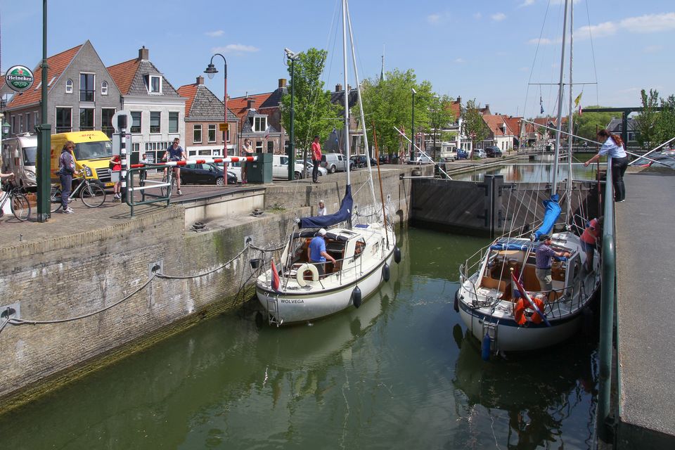 Een sluis in Makkum met twee zeilboten. aan de zijkant van de sluis staat een vrouw met een klompje om geld aan te pakken.
