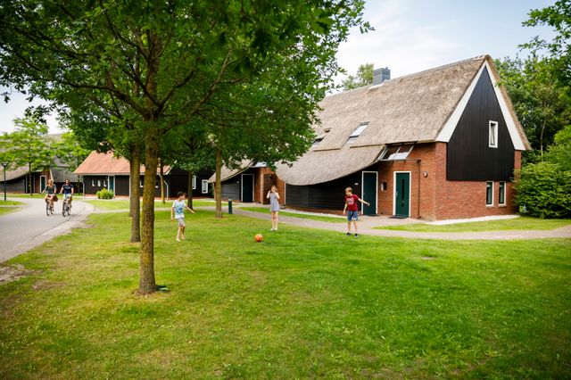 Vakantiebungalows met een grasveldje waar kinderen op voetballen.