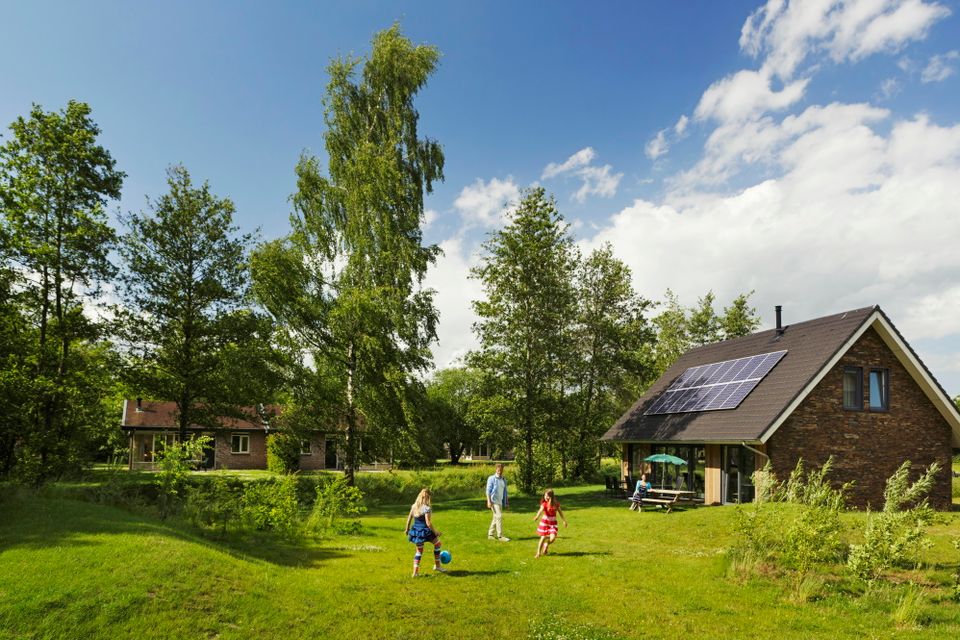 Kinderen voetballen op het grasveldje naast een bungalow.